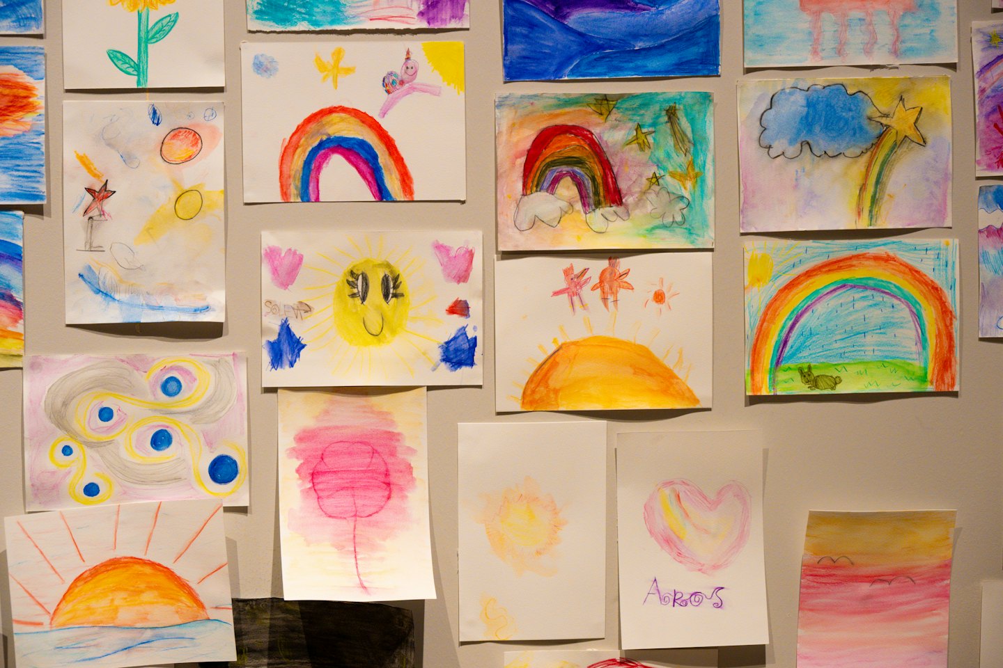 Children's colorful drawings of rainbows and suns on a wall.